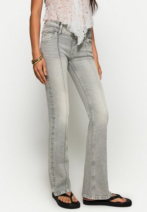 Helle grau ausgestellte Jeans mit leicht ausgebleichtem Finish, fünf Taschen-Design und Steppnähten, kombiniert mit schwarzen Flip-Flops.