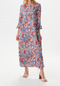 Robe longue à fleurs avec un motif vibrant en rouge, bleu et rose. Fabriquée en tissu léger, avec des manches trois-quarts et des poignets à volants.