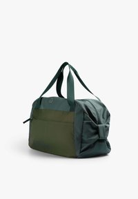 Grüne Stoff-Reisetasche mit zweifarbigem Design, ausgestattet mit einer Reißverschlusstasche vorne, stabilen Griffen und einem geknoteten Akzentdetail.