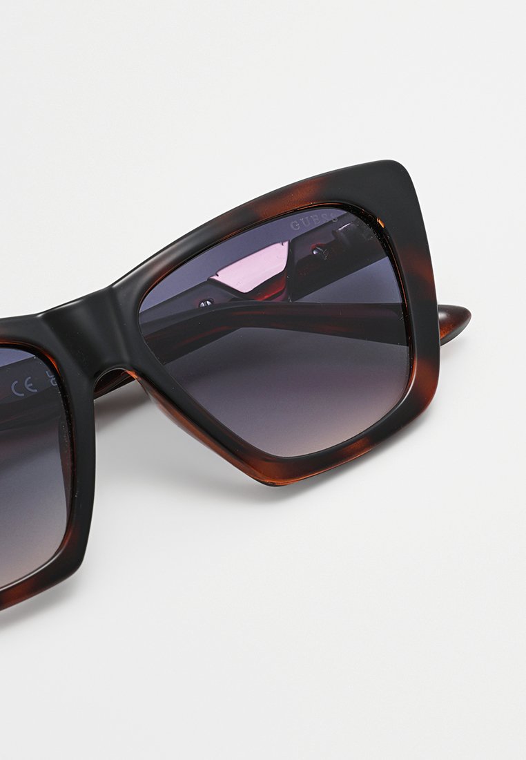 Lunettes de soleil écaille de tortue avec une monture large et angulaire et des verres dégradés passant de teintes foncées à plus claires.