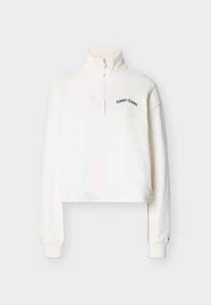 Balts garām piedurknēm kvartāla rāvējslēdzēja svīteris ar uzrakstu "TOMMY JEANS" kreisajā krūšu daļā un ribota auduma aprocēm, attēlots uz vienkārša fona.