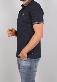 Laivastonsininen poolopaita, jossa geometrinen kuvio, kontrastiväriset raidalliset kauluksen ja hihojen reunat sekä kirjailtu logo rinnassa; slim fit-malli.