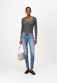T-shirt gri cu mâneci lungi și butoane la guler, blugi skinny albaștri, pantofi negri slip-on și o geantă de umăr gri deschis. Design simplu.
