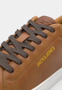 Bruine leren sneaker met donkerbruine veters, witte zool en geperst merklogo in het geel. Glad oppervlak met een strakke, moderne uitstraling.