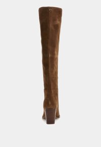 Bottes en daim marron hauteur genou avec un talon épais et un subtil détail en G au sommet. Texture lisse et design ajusté qui épousera la jambe.