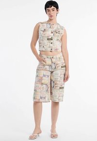 Kurz geschnittene Weste und Shorts aus Stoff mit einem Vintage-Geldschein-Muster in Pastellfarben. Das Outfit umfasst vordere Knöpfe und Taschen.