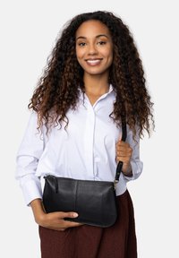 Borsa a pochette in pelle nera con finitura testurizzata, chiusura con zip e tracolla removibile. Il modello tiene la borsa contro uno sfondo bianco.