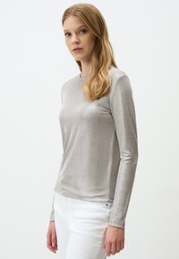 Silbernes Langarmoberteil aus einem weichen, glänzenden Material. Verfügt über einen runden Halsausschnitt und eine figurnahe Silhouette, kombiniert mit weißen Hosen.