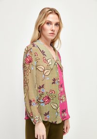 Blusa con stampa floreale che presenta una combinazione di colori verde e rosa, chiusura frontale con bottoni e maniche lunghe con colletto. Tessuto leggero e semi-trasparente.