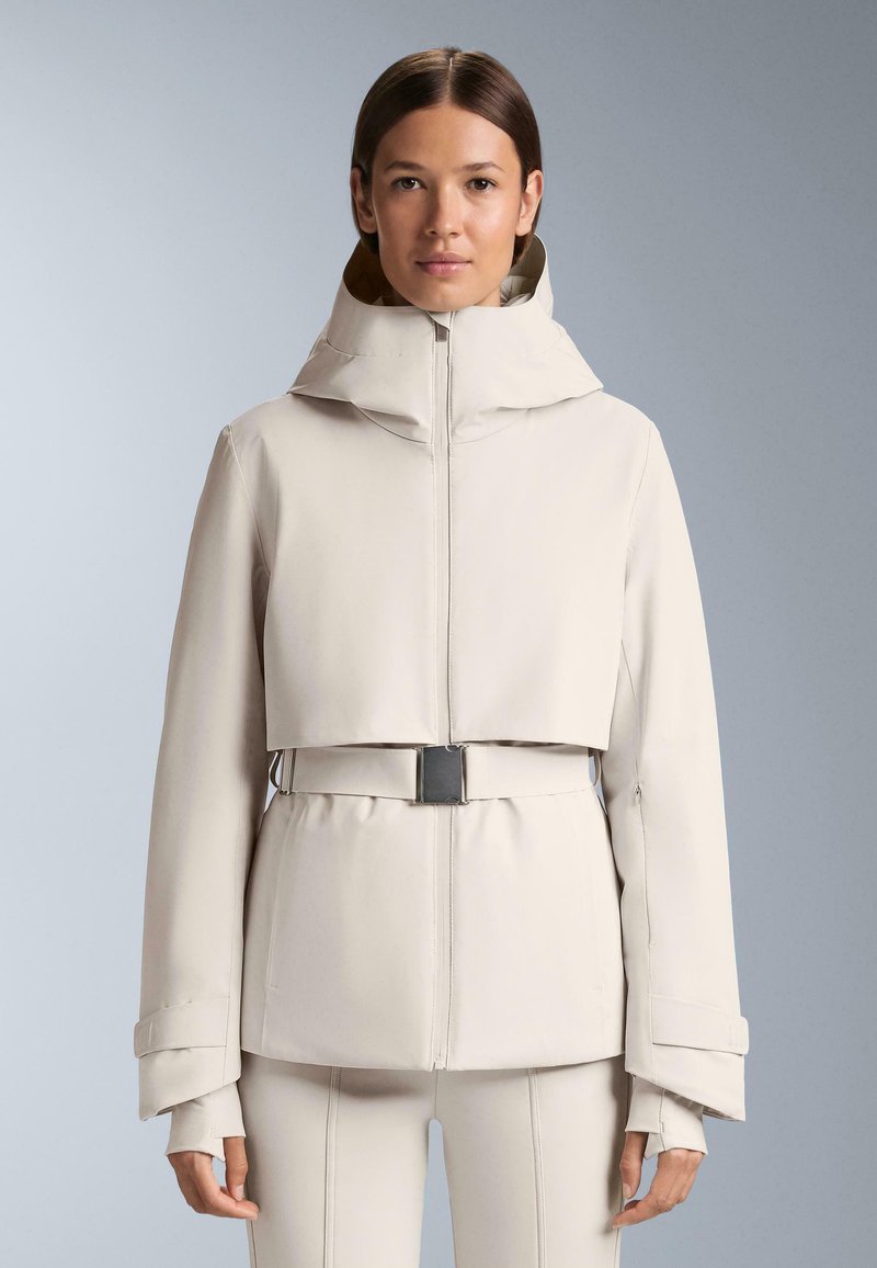 Bež jakna skraćena do struka s oblikovanim kapuljačom, zatvaranjem na patentni zatvarač i pojasom u struku. Ima široke rukave i glatku, teksturiranu tkaninu.