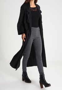 Černý oversized kabát, přiléhavý černý top s krajkou, šedé legíny a černé kotníkové boty s masivním podpatkem. Hladké, strukturované textury.