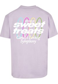Lilac short-sleeve t-shirt featuring large white text "sweet treats" and "Candy's Loving Symphony" with colorful concentric ovals as accents.