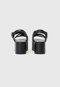 Svarte plattform sandaler med bred blokkheel, lærremmer og en gullspenne. Jevn tekstur og minimalistisk design.