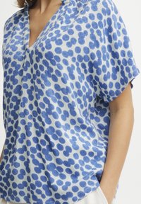 Blusa blu e bianca a pois realizzata in tessuto leggero, con scollo a V e vestibilità ampia, caratterizzata da maniche corte e un design rilassato.