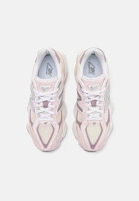 Light pink and cream sneakers with mesh panels, white laces, and silver accents. Rounded shape and textured material throughout.