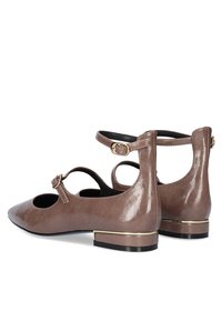 Bailarinas de charol marrón con punta redonda, tira al tobillo y tacón bajo, que presentan una banda de acento dorado y detalle lateral con corte.