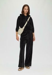 Zwart velours loungewear set met een hoodie en brede broekspijpen. Gecombineerd met een crèmekleurige schoudertas en metallic platform sneakers.