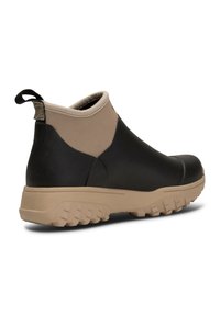 Bottines noires et beiges en caoutchouc imperméable, avec une semelle texturée et un dessus semblable à du néoprène, équipé d'une languette à l'arrière.