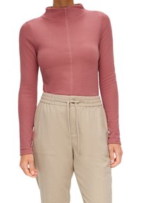 Pitkähihaista yläosaa pölyruusunvärisestä ribbikankaasta, jossa on korkea kaulus ja sauman yksityiskohtia, yhdistettynä beigeihin elastisiin housuihin, joissa on taskut.