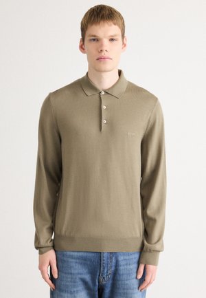Long-sleeve olive green polo shirt with a collar, three-button placket, and ribbed cuffs, paired with light blue jeans.