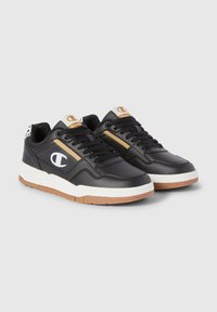 Sneakers in pelle nera con accenti bianchi e beige, con chiusura a lacci, area della punta perforata e suola in gomma naturale. Presentano un logo distintivo.