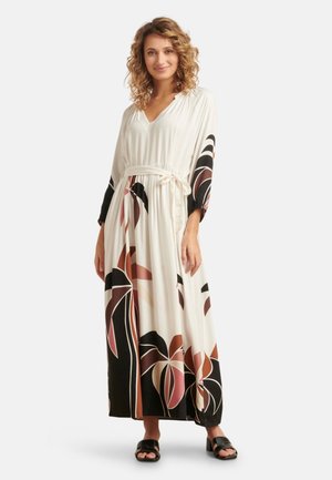 Maxikleid mit V-Ausschnitt, tailliertem Bund, langen Ärmeln, schwarzen und beigen Blumenmustern, aus leichtem Stoff. Schwarze Sandalen.