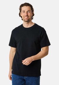 Black cotton t-shirt with short sleeves, crew neck, and a straight cut. Notable stitching detail around the collar and bottom hem.