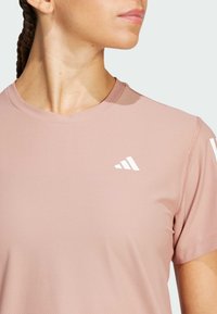 Lichtroze sportshirt van een gestructureerde stof, met een ronde halslijn en witte logo-accenten op de bovenste linker- en rechtermouwen.