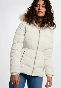 Giacca a foderato beige chiaro con cappuccio, dotata di un bordo in pelliccia sintetica, zip frontale, tasche laterali e polsini a coste. Design trapuntato equilibrato.