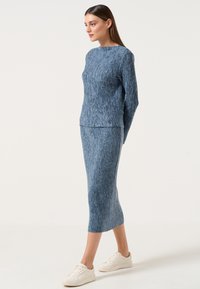 Set di maglie a due pezzi in blu con texture a costine. Maglione a maniche lunghe con scollo rotondo e gonna aderente alla lunghezza del ginocchio. Indossati scarpe bianche.