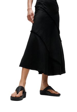 Vrouw draagt een zwarte midi-rok met lagen en zwarte sleehakken met brede, gestructureerde banden.