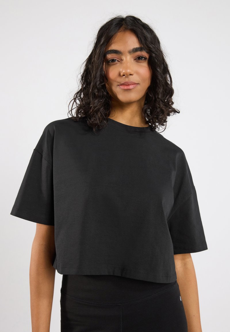 Musta lyhythihainen crop-top, joka on valmistettu pehmeästä kankaasta. Yksinkertainen muotoilu, jossa ei ole näkyvää tekstiä tai kuvioita.