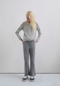 Camisa de manga larga a rayas con los hombros al descubierto, combinada con jeans de campana grises y zapatillas negras. Diseño simple y casual en materiales suaves.