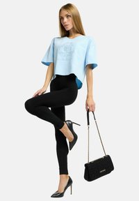 Lichtblauw cropped T-shirt met korte mouwen, zwarte legging, zwarte hoge hakken, en een zwarte textuur handtas met een gouden kettingband.