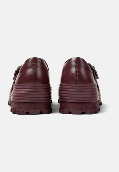 Burgundy leather shoes with a textured, ridged sole. Rounded back with lace-up detail and smooth finish on upper.