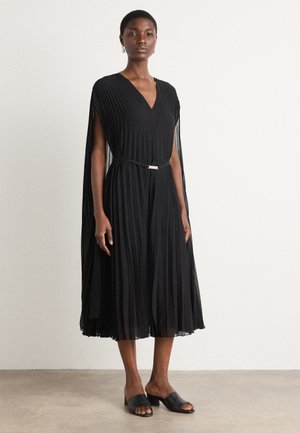 Black pleated dress featuring a V-neck and flowing cape sleeves, cinched at the waist with a thin silver belt. Smooth fabric finish.