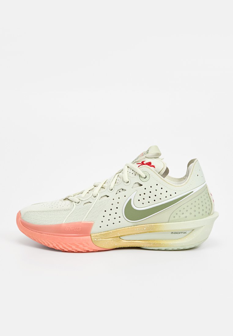 Chaussure de sport Nike avec un empeigne en mesh beige clair, des perforations, un swoosh vert, des accents de semelle rose et jaune, et un design rembourré.