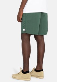 Groene stoffen short met een ontspannen pasvorm, zijzakken en een merklabel aan de onderzijde links. Draagt bij lichte suède schoenen.