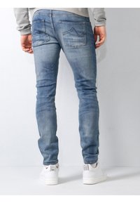 Jeans din denim albastru cu croi slim și spălare deschisă. Prezintă două buzunare pe spate cu detalii de cusătură curbată, textură uzată și un finisaj neted.