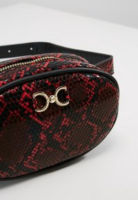 Borsa a tracolla con motivo in pelle di serpente nera e rossa, chiusura e dettagli con cerniera in metallo dorato. Texture liscia, forma arrotondata, tracolla flessibile.