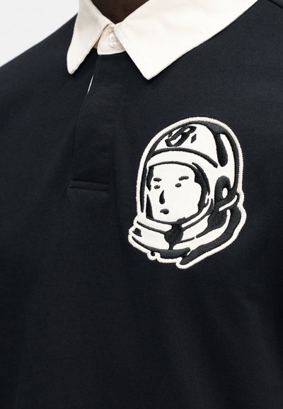 Μαύρο πόλο μπλουζάκι με γιακά σε εκρού χρώμα και έντονο κεντητό σχέδιο κράνους αστροναύτη σε λευκό και μαύρο.