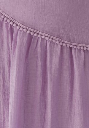 Tissu lavande froissé avec une bordure diagonale en dentelle de pompons séparant la section supérieure lisse de la section inférieure froncée.