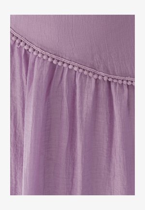 Ljubičasta naborana tkanina s dijagonalnim obrubom od sitne čipke s pomponima koja odvaja glatki gornji dio od nabrane donje sekcije.