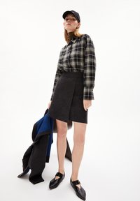 Camicia a maniche lunghe a quadri in bianco e nero; gonna avvolgente grigio scuro, fino al ginocchio; cappellino nero; scarpe nere con cinturino.