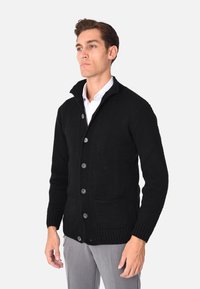 Cardigan nero lavorato a maglia con un motivo testurizzato, chiusura a bottoni e due tasche anteriori, caratterizzato da un colletto ripiegato e polsini a coste.