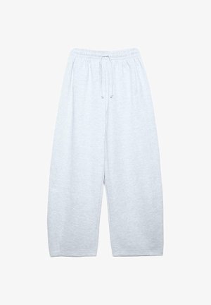 Personne portant un haut côtelé gris à manches longues, un pantalon de survêtement gris clair oversize, des chaussures noires et un pull bleu drapé sur les épaules.