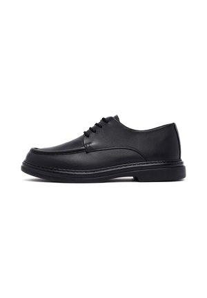 Black leather men's dress shoe with lace-up closure and thick sole, shown from the side on a white background.