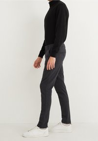 Černé tričko s dlouhým rukávem a rolákem v kombinaci s tmavě šedými kalhotami. Kalhoty mají jemný vzor a detail zadní kapsy. Bílé tenisky.