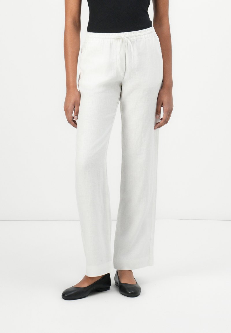 Light gray linen trousers with a relaxed fit, elastic waistband, and drawstring. Paired with black flat shoes. Smooth, textured fabric.