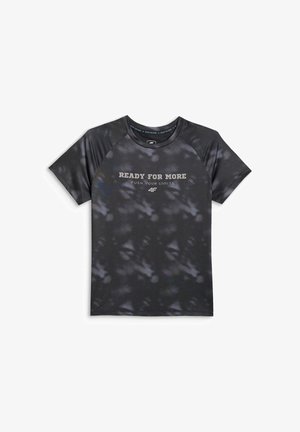 Chłopiec stoi prosto, ubrany w czarną koszulkę tie-dye z tekstem "Ready for More", czarne szorty, białe skarpetki w paski i czarno-białe trampki.